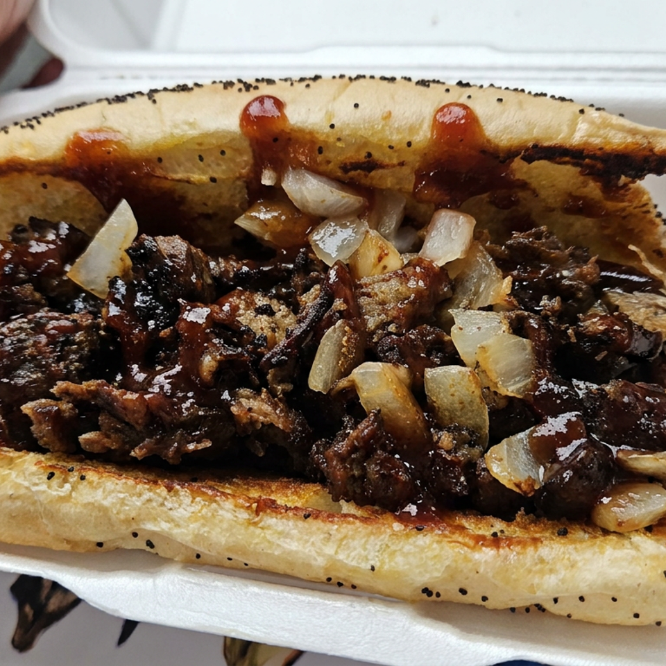 Grilled pita sandwich filled with chopped meat, caramelized onions, and brown sauce, served in a white takeaway container.