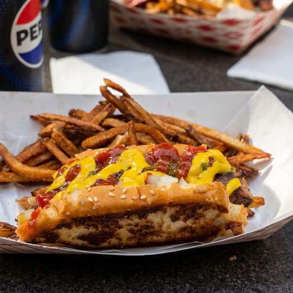 Cheeseburger topped with ketchup, mustard, onions, and pickles served with fries, Pepsi, and napkins on a restaurant table.